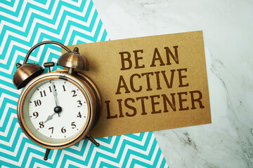 Be An Active Listener text written on paper card with alarm clock on marble background