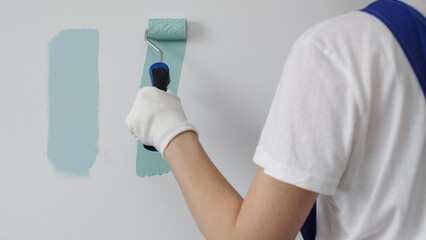 Professional painter holding paint roller, comparing light green paint shades, selecting precise wall color for home renovation, ensuring ideal interior design aesthetic