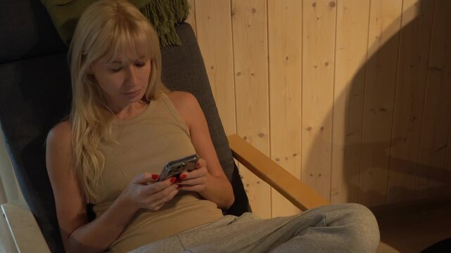 A young woman is sitting in a chair. A girl is resting, looking at her phone.