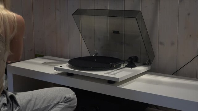A girl listens to music on a vinyl record player. A young woman places a vinyl record on the player.