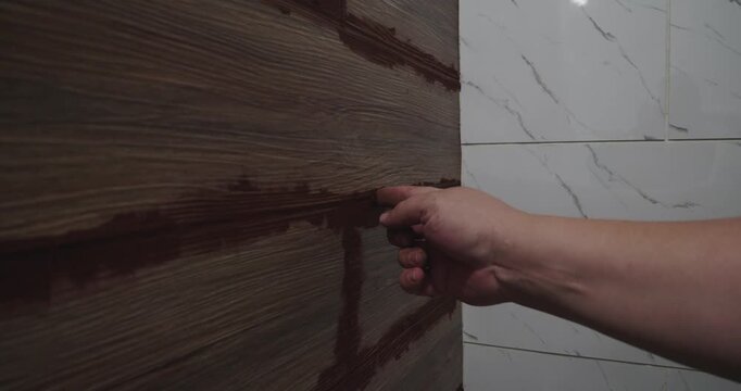 Skilled worker's hand carefully applying dark grout between wood-look ceramic wall tiles. Close-up view of home renovation, focusing on the meticulous process of filling the joints.