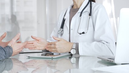 Doctor consulting patient, discussing diagnosis, using digital tablet in modern medical clinic. Medicine and health care