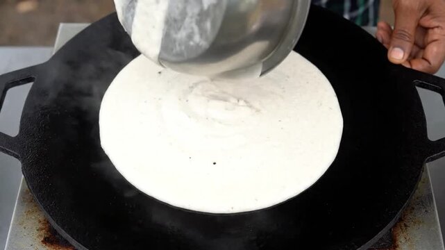 Chef making a perfect dosa on a hot tawa in a continuous top-down shot