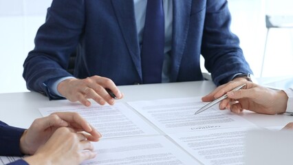 Business people or lawyers reviewing and discussing contract while gathering in a bright office...