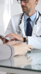 Male doctor consulting female patient, discussing diagnosis and medical history with digital tablet in clinic. Medicine and health care