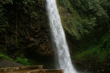 Fototapeta premium A beautiful natural scene showing the base of a waterfall as it flows into a dark rocky pool surrounded by wet stones and lush greenery. The mist and motion of the water create a sense of freshness an