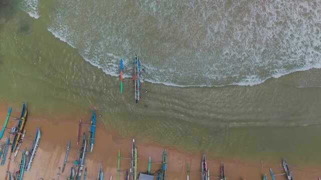 Aerial View of Fishermen Launching Traditional Fishing Boat into Ocean Waves