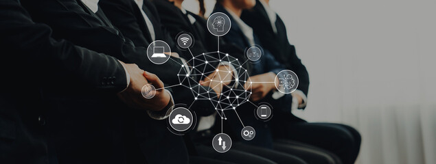 A group of business professionals dressed in suits sits attentively during a meeting. Digital icons showcase themes of technology and collaboration, illustrating modern business dynamics. Trope