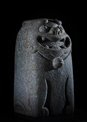 Ancient stone lion statue with intricate carvings on a black background.