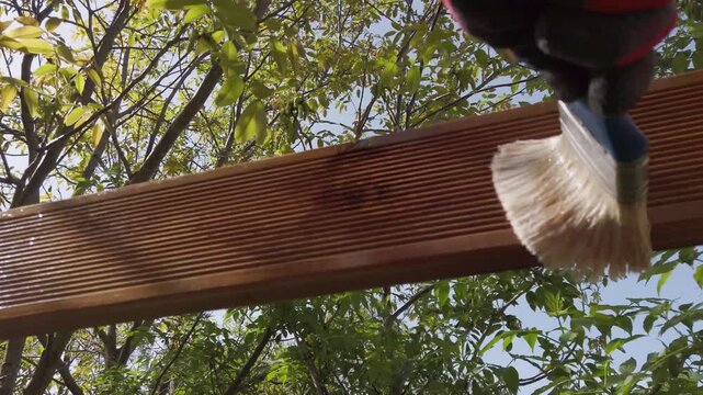 Hand in glove painting fence of impregnated ship floor planks. Carpenter applying protective layer of varnish.
