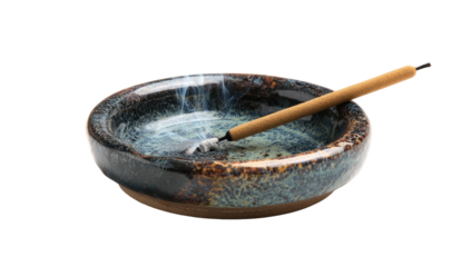 Incense stick burning in a small blue speckled ceramic dish, isolated against a black background