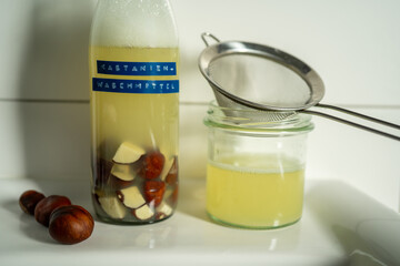 A glass bottle filled with homemade liquid detergent made from horse chestnuts and water. Sustainable alternative to commercial laundry detergents with visible German label.
