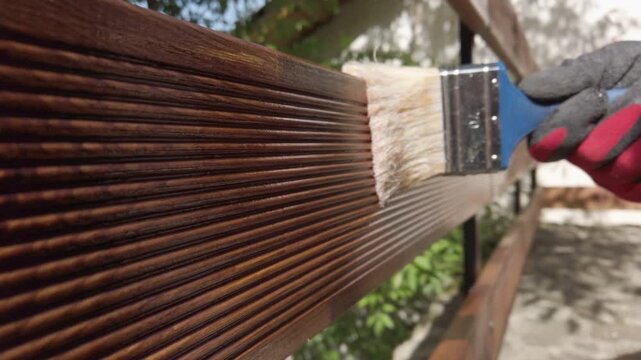 Hand in glove painting fence of impregnated ship floor planks. Carpenter applying protective layer of varnish.