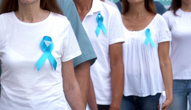 A united group of people wearing white shirts with light blue awareness ribbons to support a health cause.