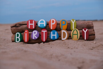 Creative Happy Birthday message composed with hand painted multi colored stone letters on the beach