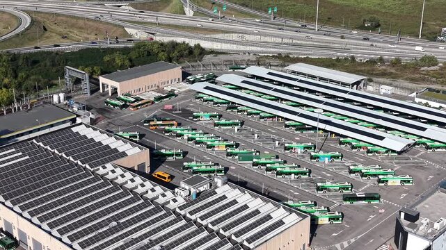 Bus Depot Aerial View. An expansive aerial view showcases a meticulously organized bus depot, revealing a grid of stationary public transportation vehicles awaiting their next journey.