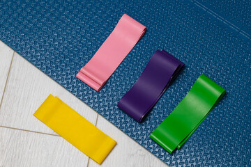 Colorful resistance bands in vibrant shades of pink, purple, green, and yellow, arranged on a textured blue exercise mat, showcasing fitness equipment for strength training and physical wellness