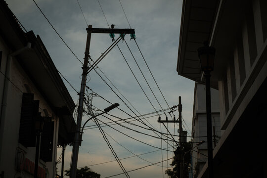 Silhouette of tangled power lines and electric poles during dusk, depicting urban infrastructure and evening city atmosphere. - Powered by Adobe