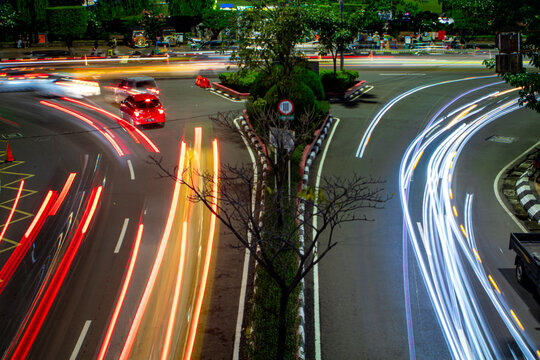 Long exposure photo of car light trails at a city intersection at night, showing motion, energy, and modern urban lifestyle.