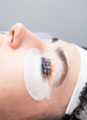 Close-up of an eye with a silicone roller under a film during an eyelash lamination procedure and patches. Beauty salon beauty treatments