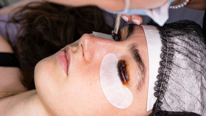 A close-up of a cosmetologist applying a laminating compound to a client's eyelashes. Beauty salon beauty treatments.