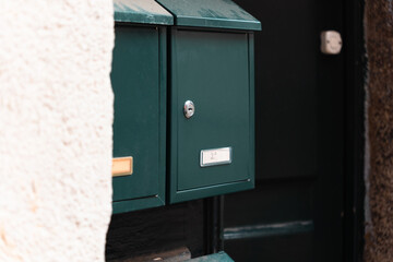 Green mailbox stands out near a rustic stone wall on a quiet street at midday
