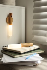 Stack of notebooks on pouf and portable LED lamp at home