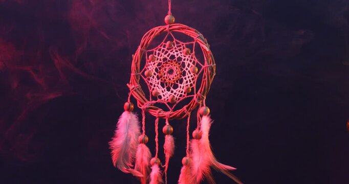 Beautiful dream catcher hanging in color lights on dark background with smoke