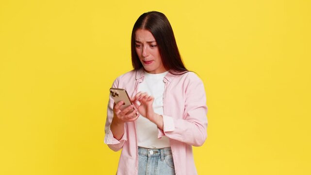Woman panicking frantically tapping on smartphone screen, reacting in fear after accidentally deleting something important. Girl on yellow background shows emotional stressful gesture of digital panic