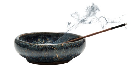 Incense stick burning over a speckled bowl, smoke rising, against a black background