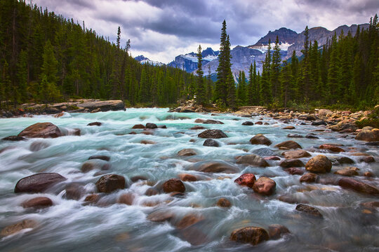 Rushing River and Rocky Stream with Mountain Peaks and Dense Evergreen Forest