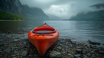 Red kayak on rocky shore, misty fjord mountains.