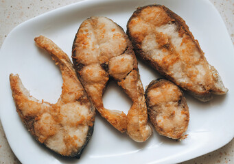 Pieces of fish fried in vegetable oil lie on a white plate. Concept for breakfast, lunch, or dinner.