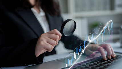 A business professional examines stock market trends using a magnifying glass on a laptop. Financial graphs overlay the scene, representing analysis in a modern office. Impute