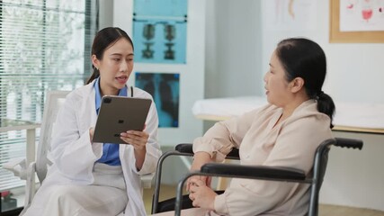 Smiling Asian female doctor talking with senior female patient in a wheelchair while taking notes on a digital tablet in a modern clinic, showing care, trust, and technology in healthcare. - Powered by Adobe