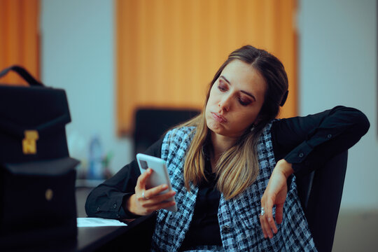Bored Office Worker Checking her Phone Sitting at Desk. Lazy procrastinator employee being distracted by doom scrolling