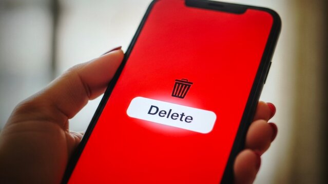 Closeup of a hand holding a smartphone with a red screen showing a delete button and trash can icon
