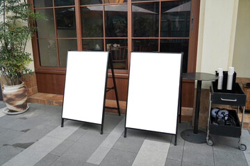 Blank white outdoor advertising or stand sandwich board mock up template. Clear street signage board placed by an outdoor dinning area of a restaurant.