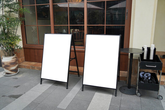 Blank white outdoor advertising or stand sandwich board mock up template. Clear street signage board placed by an outdoor dinning area of a restaurant.
