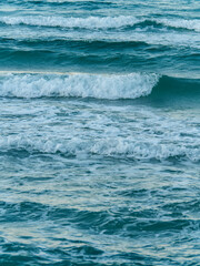 A vertical photograph of the beautiful open sea with multiple lines of waves rolling towards the shore creating a serene and rhythmic pattern