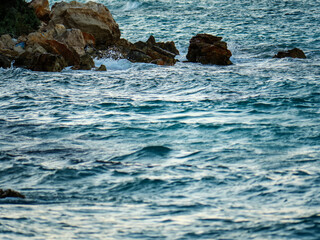 A dramatic photograph of large choppy sea waves crashing against a rocky coastline creating a powerful display of water and stone
