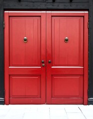 Fototapeta premium Symmetrical view of vibrant, red wooden double doors with brass hardware