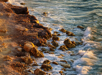 A beautiful and rugged coastline with rocky shores and sandy beaches being hit by gentle sea waves during the warm light of golden hour which illuminates the scene