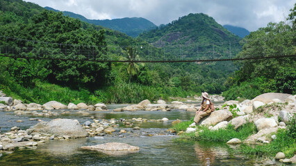 A woman sitting on the rock by the creek with forest and mountain views