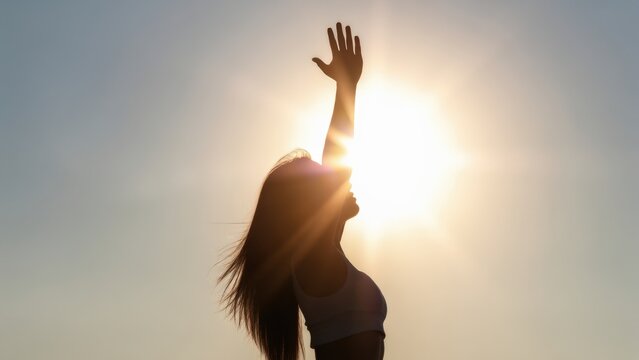 Strong confident woman! Winning and life goals concept. Silhouette of a woman reaching towards the sun against a bright sky.