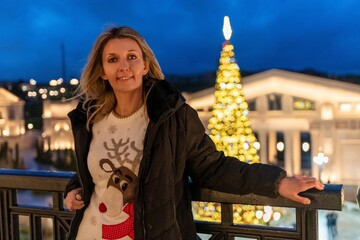 Woman christmas sweater portrait, smiling adult enjoying festive urban view at winter night