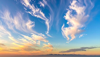 Wispy clouds in vibrant, blue sky with sunset hues near horizon