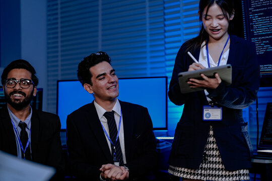 Software engineers and data scientists analyze AI code. An Asian female programmer holds a tablet while her Caucasian and Indian male colleagues discuss the system.