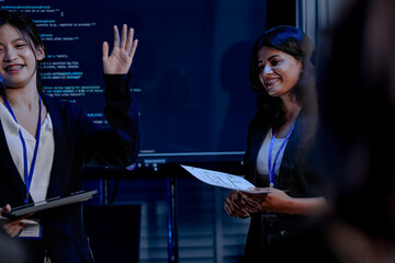 An Indian female developer leads a code review, holding a report. She explains a Python script for an AI or cybersecurity system to her team in a dark SOC Security Operations Center