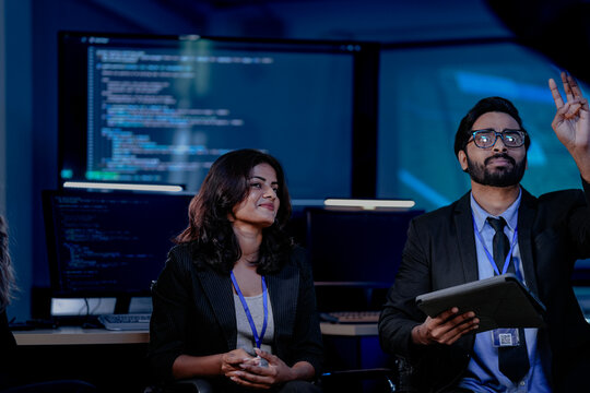 A diverse IT team, including an Indian man and woman, in an urgent security briefing. They are focused, listening to an update on a critical data incident or system failure.